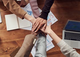 Diverse professionals unite for teamwork around a wooden table with laptops and documents.